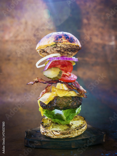 Hamburger with realistic flying ingredients. Tasty smoked grilled and glazed beef burger with lettuce, cheese and bacon on wooden table with copyspace.