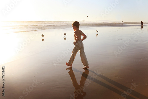 Boy Holding Pants Legs Up Walking Towards Ocean photo
