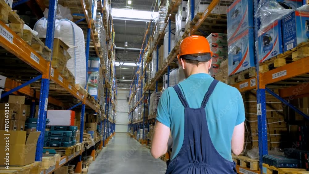 A back view on a warehouse employee walking an aisle at a storage. 4K. A back view on a warehouse employee walking an aisle at a storage. 4K.