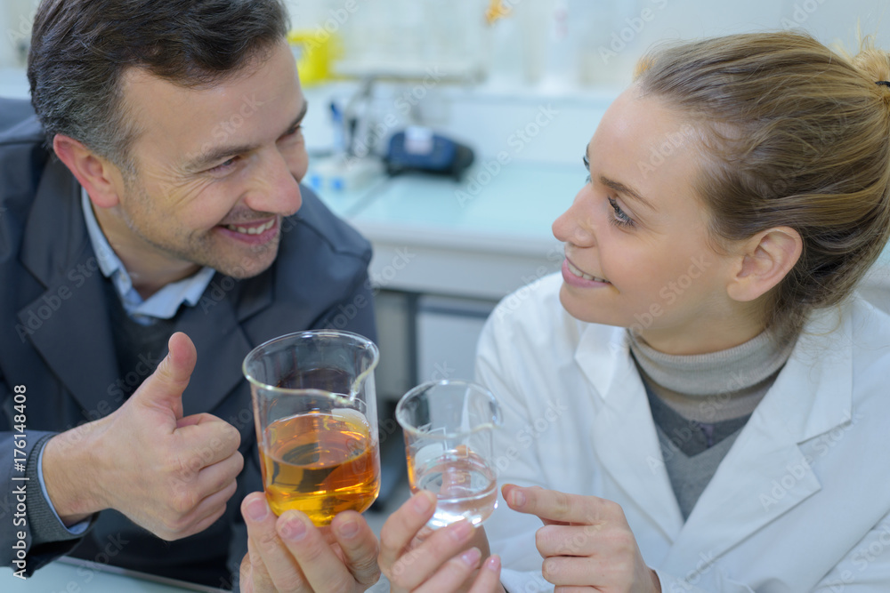 Man and woman comparing liquids in glass beakers Man and woman comparing liquids in glass beakers