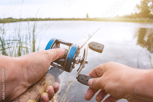 A man is fishing with a baitcasting reel. Hands, a rod and a baitcasting reel in the background of the rising sun photo