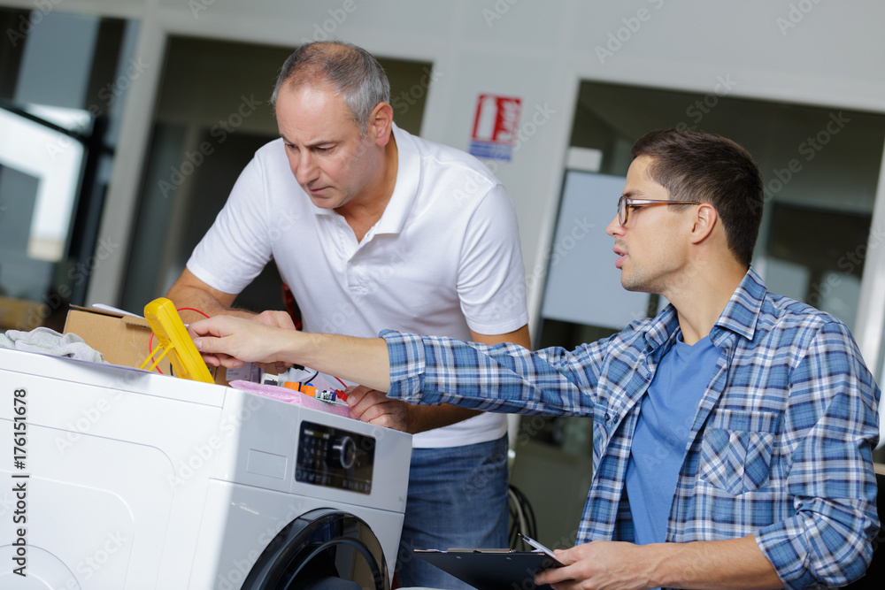 two plumber with clipboard fixing a washing machine two plumber with clipboard fixing a washing machine