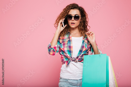 Pensive serious woman talking on phone and holding bags isolated