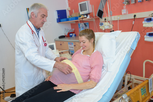 Doctor putting foetal monitoring belt on pregnant lady photo