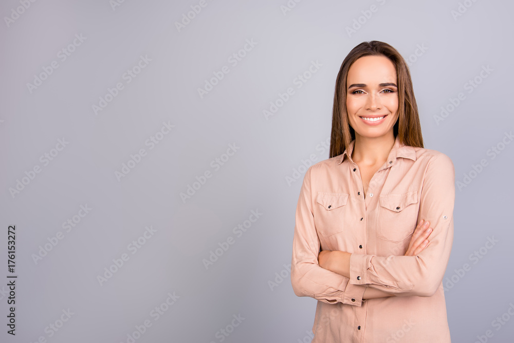 Portrait of beautiful smiling young business lady in a beige smart shirt, standing on the pure background with crossed arms near copyspace Portrait of beautiful smiling young business lady in a beige smart shirt, standing on the pure background with crossed arms near copyspace