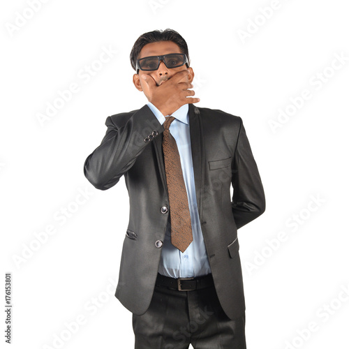 Businessman in black suit covering mouth with hand over white background © flowgics