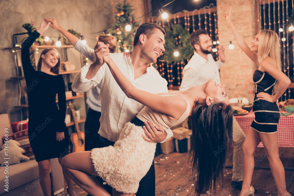 Excited, welldressed, cheerful, elegant husband holds cute wife, lean, she bending over, raised up leg, group of festive fancy luxury classy models with hot figures realx, enjoy, funky night - obrazy, fototapety, plakaty 