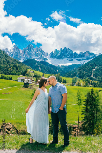 Young couple admires the view in relaxation. Famous best alpine place. Santa Maddalena village with magical Dolomites mountains in background  Val di Funes valley  Trentino Alto Adige Italy