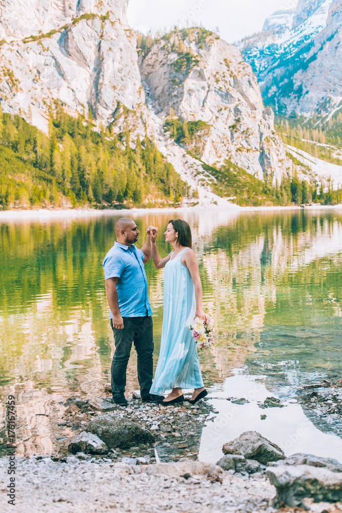 Young couple near lake lago di braies,Dolomite,Italy hold the hand stand at the stone at lake.