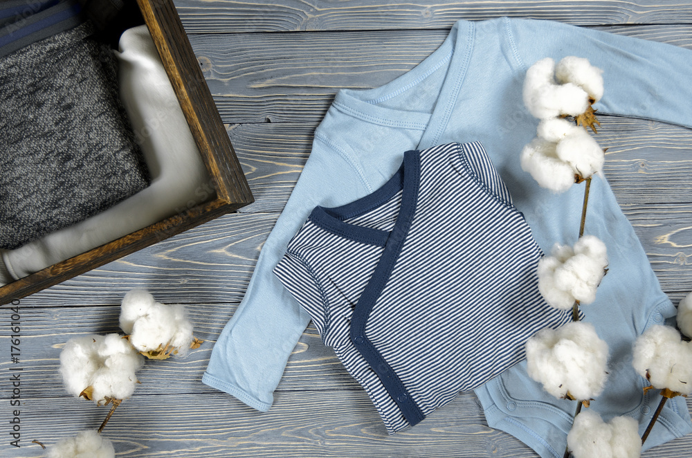 Two blue babies bodysuits on gray wooden background. Shopping maternity concept. Cotton fabric. Natural cotton stems Two blue babies bodysuits on gray wooden background. Shopping maternity concept. Cotton fabric. Natural cotton stems