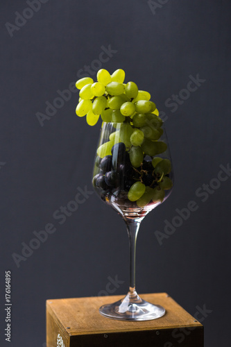 A food photo combines incompatible images. Brushes of red and green grapes in a wine glass look aristocratic and provocative. A top view of a gastronomic ecstasy photo