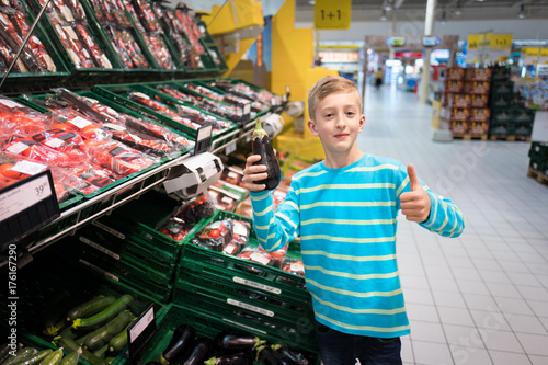 Young boy shopping eggplant in a supermarket feeling satisfied with his choice