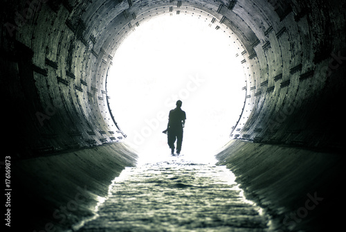 silhouette of man walking in drain tunnel
