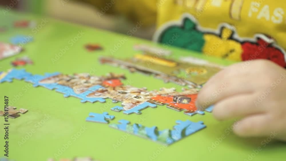 Close-up of hands of little unidentified child collecting picture from puzzles at the table in kindergarten Close-up of hands of little unidentified child collecting picture from puzzles at the table in kindergarten