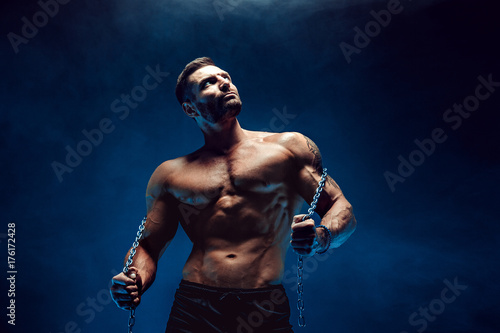 Side view of muscular bodybuilder man posingwith rope in studio, smoke. photo