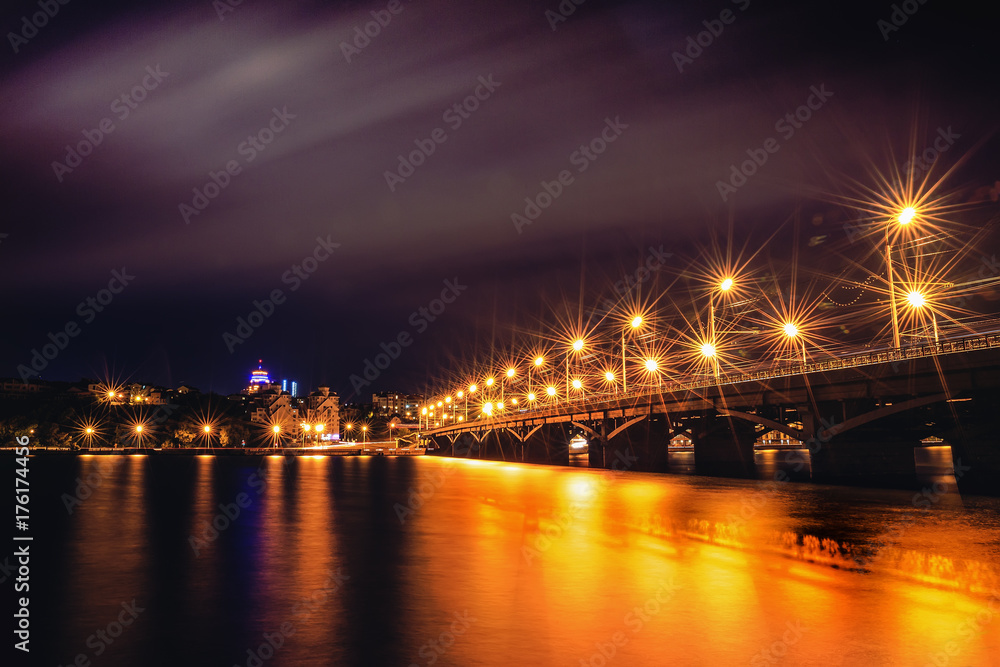 Illuminated Chernavsky bridge at night, view to right bank or downtown of Voronezh city, dramatic cityscape with reflection