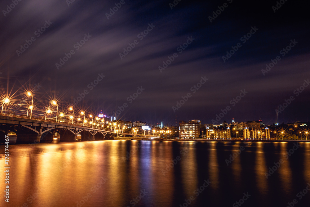 Illuminated Chernavsky bridge at night, view to right bank or downtown of Voronezh city, dramatic cityscape with reflection