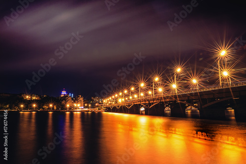 Illuminated Chernavsky bridge at night, view to right bank or downtown of Voronezh city, dramatic cityscape with reflection