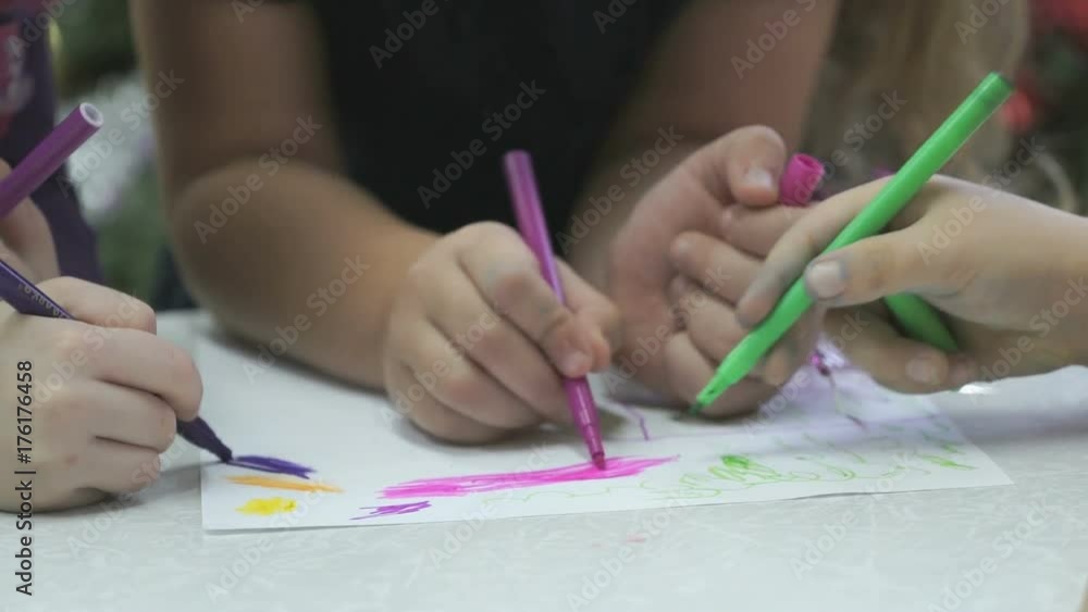 Close-up of hands of unknown little children draw and paint pictures with felt-tip sitting at desk in the kindergarten Close-up of hands of unknown little children draw and paint pictures with felt-tip sitting at desk in the kindergarten