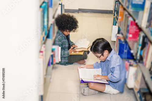 Two boy reading on the library floor. Young students study in the library. Ecucation and back to school concept. photo