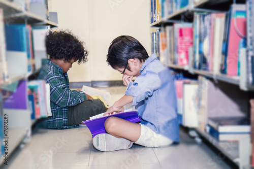 Two boys reading on the library floor. Young students study in the library. Ecucation and back to school concept. photo