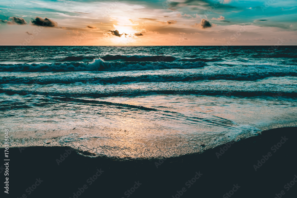bright sun rising in the colorful sky over dark sand and waves