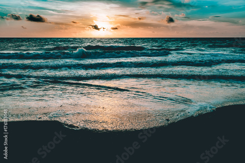 bright sun rising in the colorful sky over dark sand and waves
