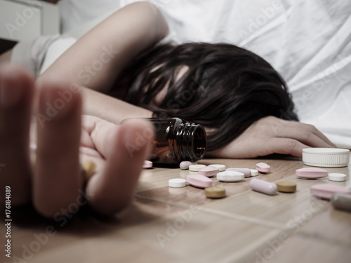 Young woman is lying on the floor with a lot of pills. Overdose and suicide concept.