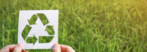 Cut paper with the logo of recycling over green grass. Recycling sign and symbol background banner concept photo