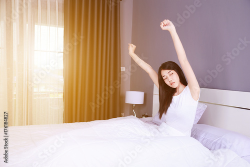 Woman waking up and hand raised on bed in bedroom