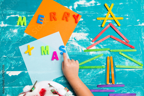 Children play plastic letters to combinations word "MERRY X MAS" .