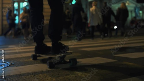 Skateboarder person feet rides across night city road busy crosswalk, crowded street