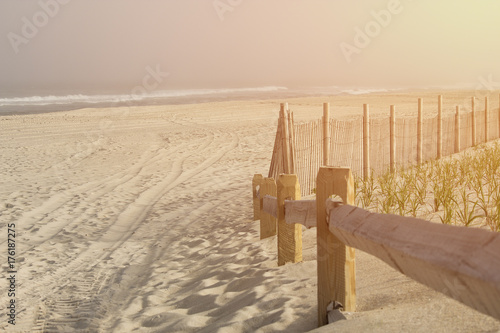 Empty beach at lonely oceanside with warm emotional bright sun pouring into the frame.  Wooden railing and waves in the distance.  Copyspace room for text.