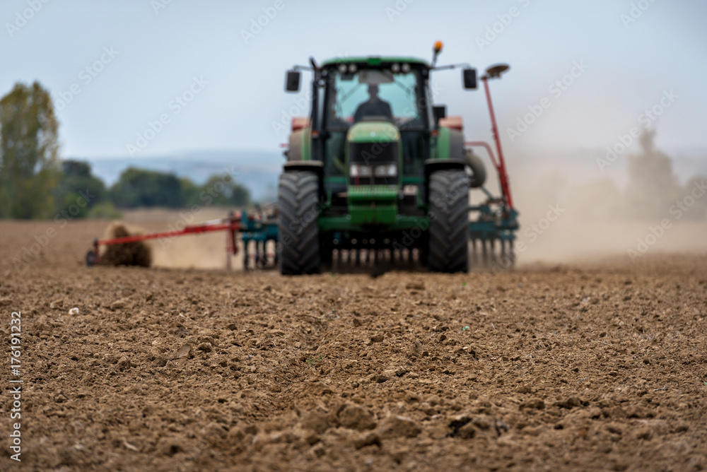 Close-up of crop with Tractor ploughing field in the background. Farmer with tractor seeding. Close-up of crop with Tractor ploughing field in the background. Farmer with tractor seeding.