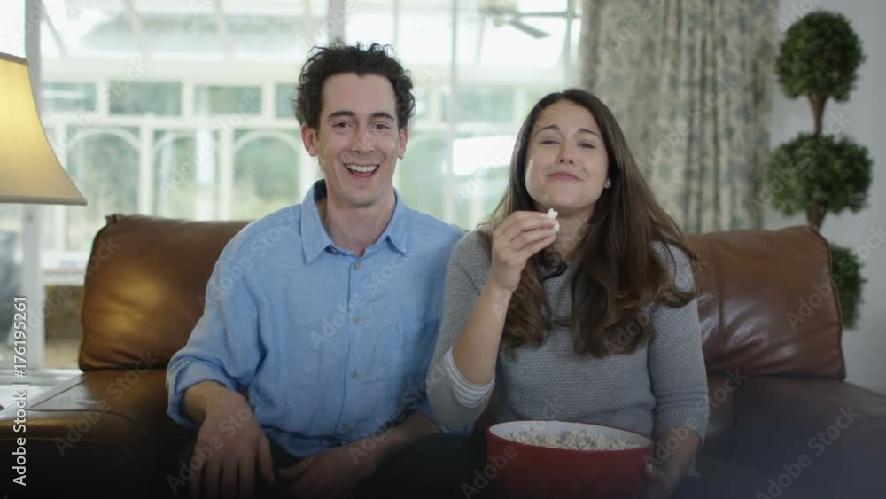 Couple watching TV & eating popcorn, laughing at the action on screen Couple watching TV & eating popcorn, laughing at the action on screen