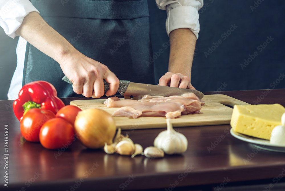 The chef in black apron cuts chicken fillet knife. Concept of eco-friendly products for cooking The chef in black apron cuts chicken fillet knife. Concept of eco-friendly products for cooking