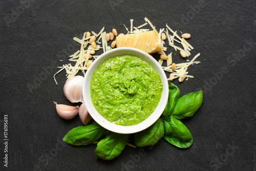 Pesto sauce in a bowl with pine nuts, parmesan and garlic over black stone background
