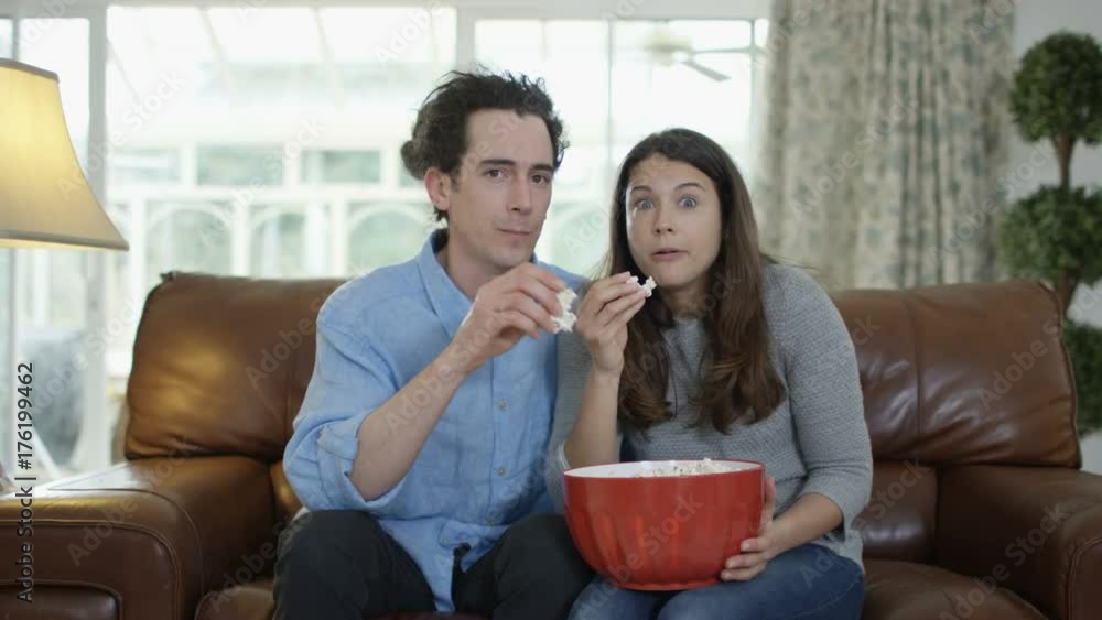 Couple watching TV & eating popcorn, shocked reaction the action on screen Couple watching TV & eating popcorn, shocked reaction the action on screen