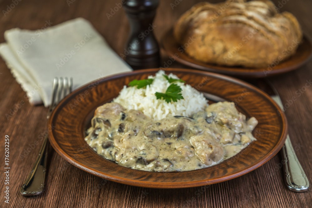 Fricassee of chicken with mushrooms with rice in a ceramic bowl on brown wooden table. Fricassee of chicken with mushrooms with rice in a ceramic bowl on brown wooden table.