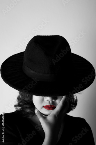 Bild auf Leinwand Beautiful young woman wearing black dress, black hat and red lips in the dark co