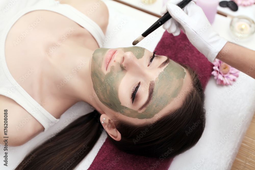 Naklejka premium Spa therapy for young woman receiving facial mask at beauty salon - indoors