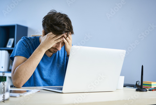 Tired young man in front of laptop in home office having headache photo