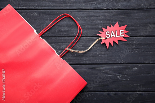 Shopping bag and red sale tag with inscription Sale on black wooden table