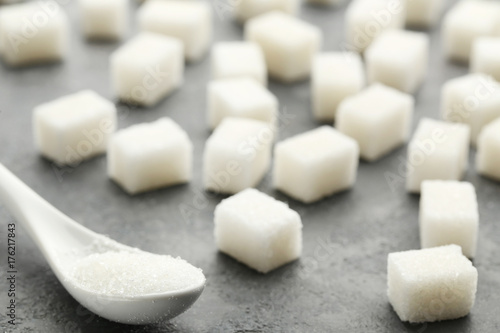 Sugar cubes with white spoon on grey wooden table