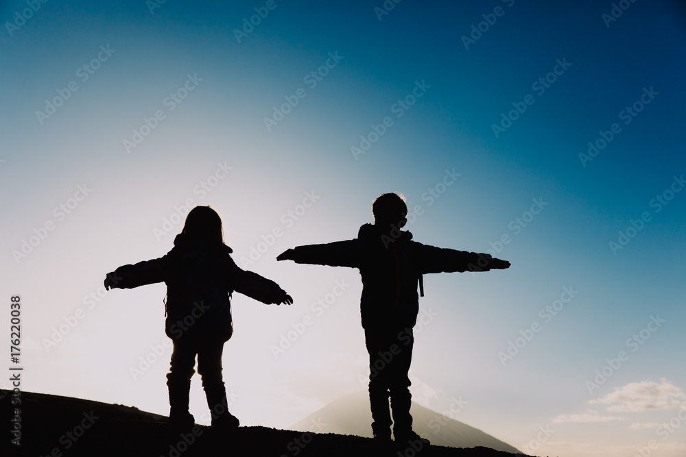 Fototapeta premium Silhouettes of little boy and girl hiking in sunset