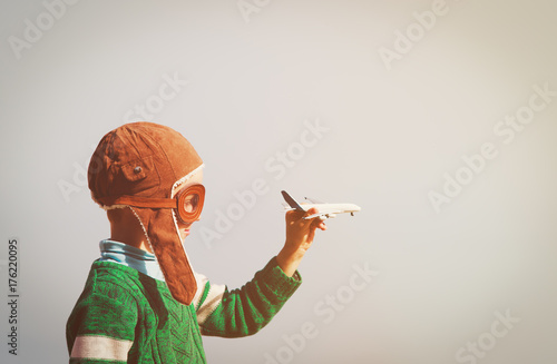Fotografija little boy with helmet and glasses play with toy plane on sky