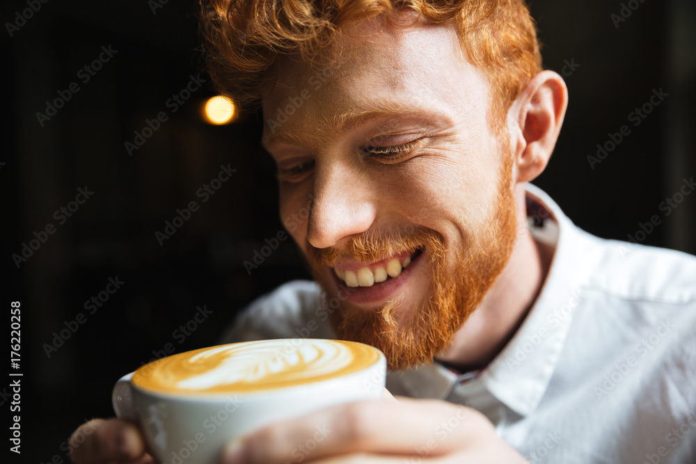 Close-up portrait of smiling curly readhead bearded man tasting coffee in cup Close-up portrait of smiling curly readhead bearded man tasting coffee in cup
