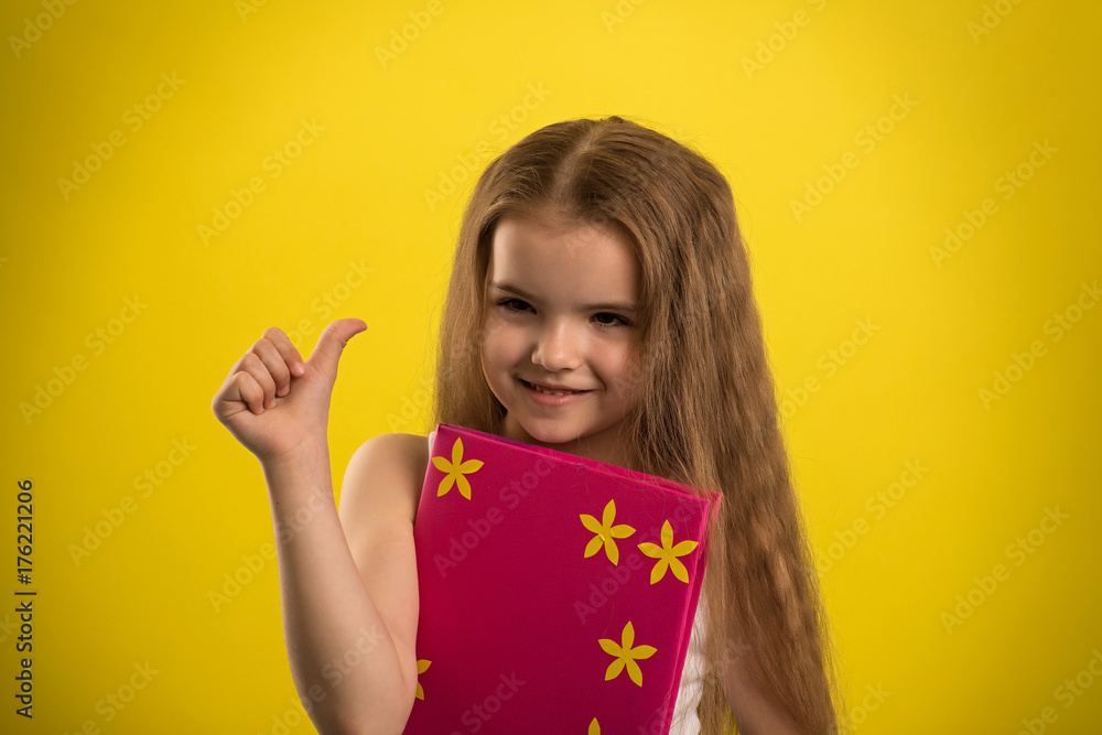 Concept - education. Girl reading a book in a pink cover, shooting in the studio on an isolated yellow background Concept - education. Girl reading a book in a pink cover, shooting in the studio on an isolated yellow background