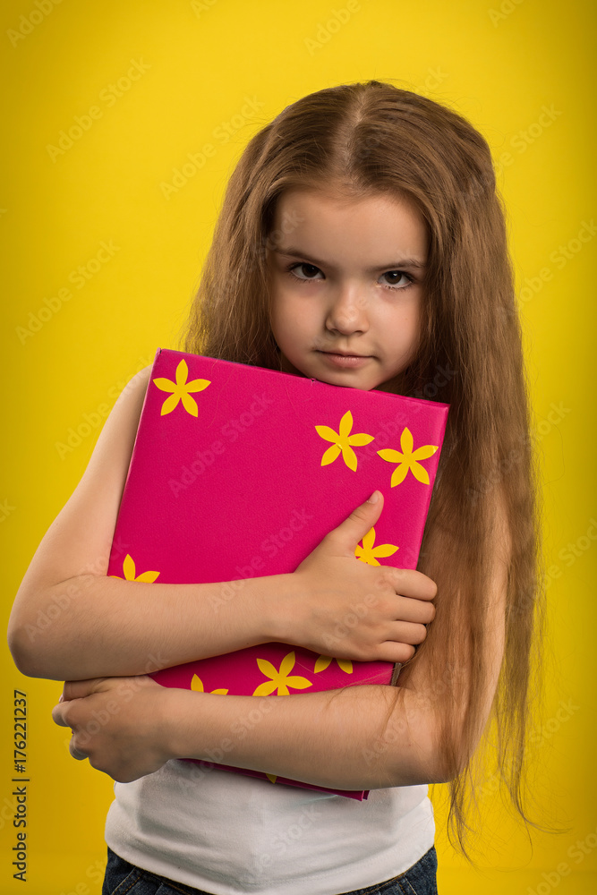 Concept - education. Girl reading a book in a pink cover, shooting in the studio on an isolated yellow background Concept - education. Girl reading a book in a pink cover, shooting in the studio on an isolated yellow background