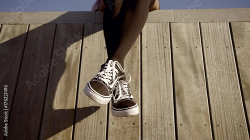 stylish young woman with dreadlocks is sitting legs crossed on a wooden fence in a city photo